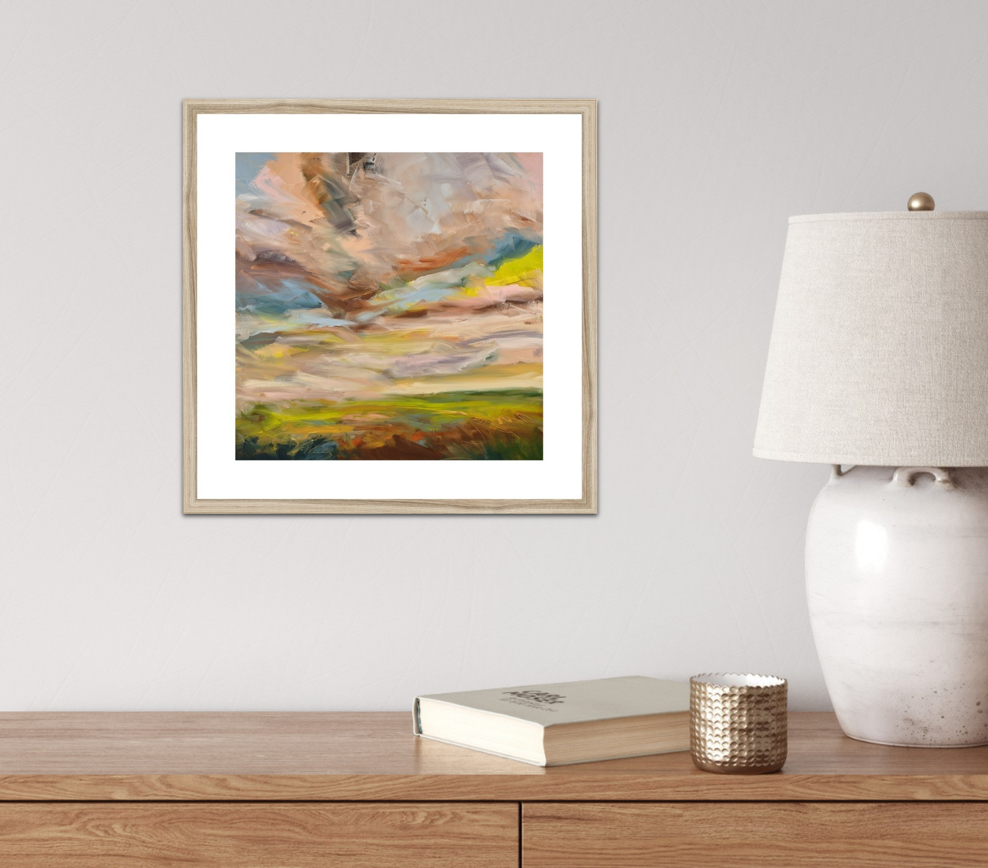 Framed abstract painting on a wall above a wooden desk with a lamp and books.