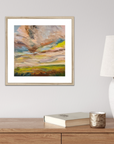 Framed abstract painting on a wall above a wooden desk with a lamp and books.
