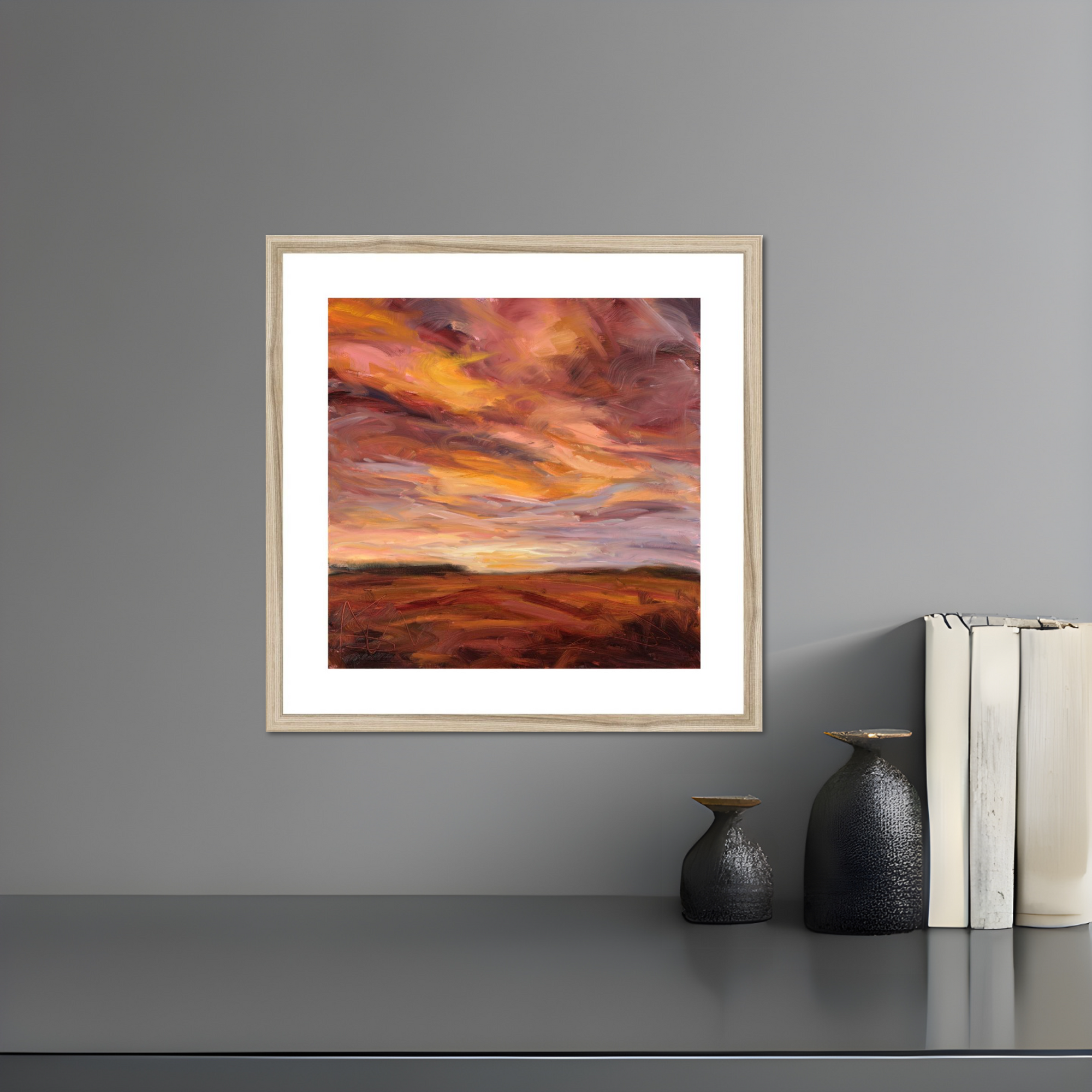 Framed artwork of a sunset over a landscape on a gray wall with decorative items below.