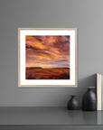 Framed artwork of a sunset over a landscape on a gray wall with decorative items below.