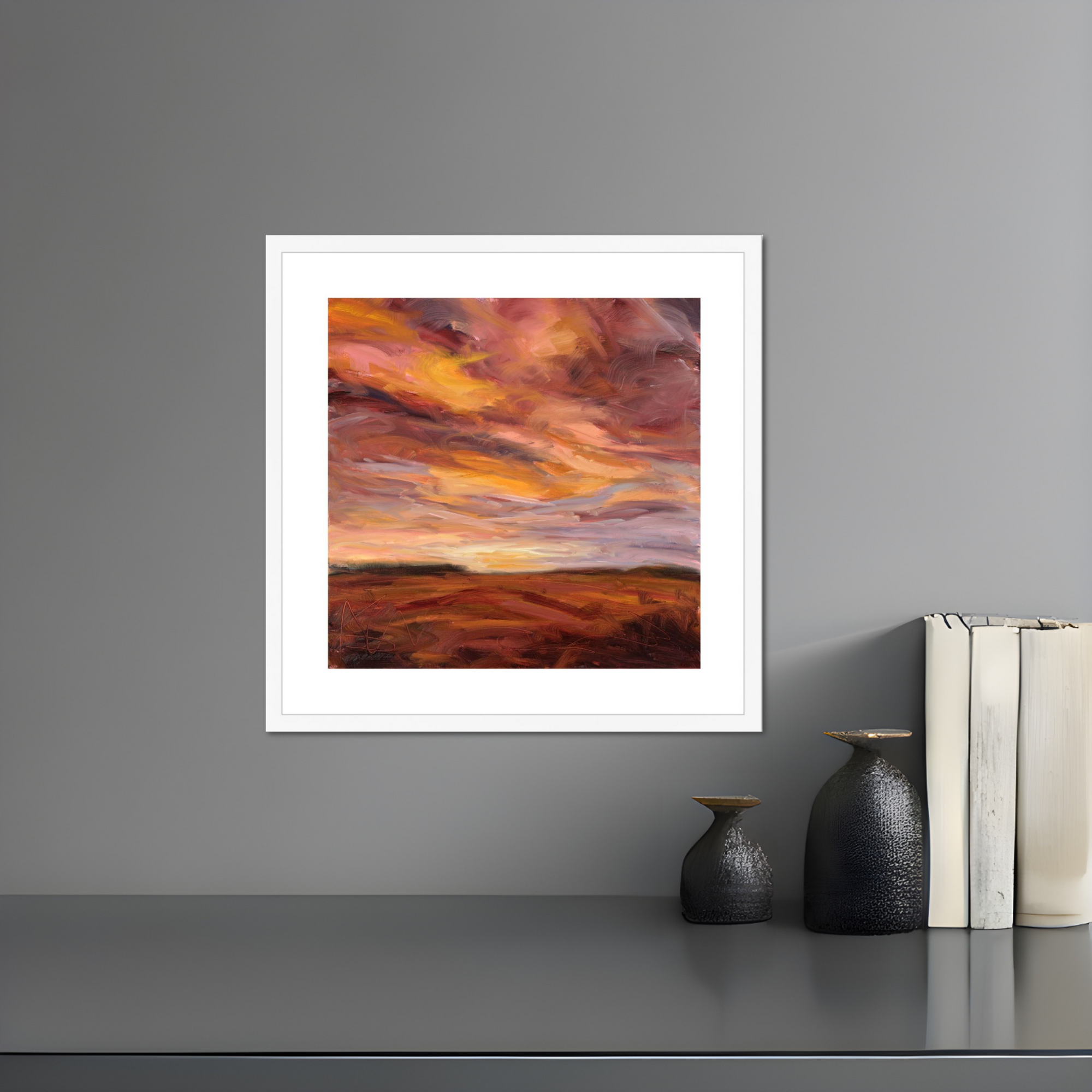 Framed artwork of a colorful sky over a landscape on a gray wall with decorative items below.