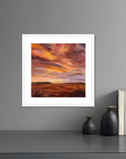 Framed artwork of a colorful sky over a landscape on a gray wall with decorative items below.
