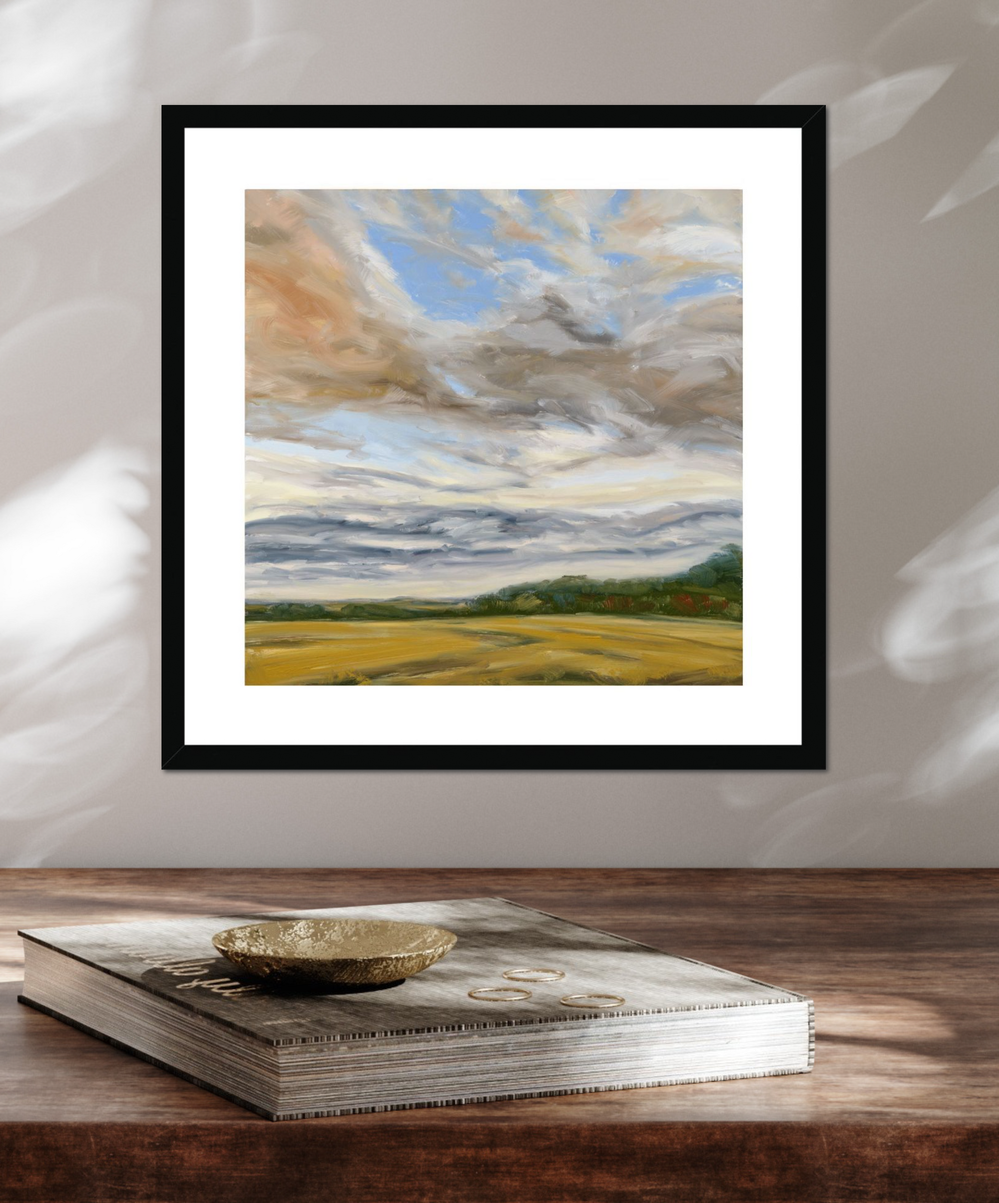 Framed landscape painting on a wooden surface with a book underneath