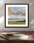 Framed landscape painting on a wooden surface with a book underneath