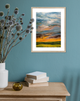 Framed artwork of a sunset over a field on a teal wall with decorative items on a wooden surface.