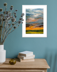 Framed artwork of a sunset over a field on a teal wall with decorative items on a wooden surface.