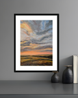 Framed artwork of a landscape with a sunset on a gray wall.