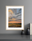 Framed artwork of a landscape with a sunset on a gray wall.