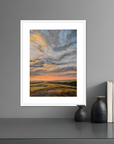 Framed abstract landscape painting on a gray wall with decorative vases and books below.