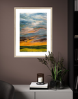 Framed abstract painting on a wall with a candle and plant on a table below.