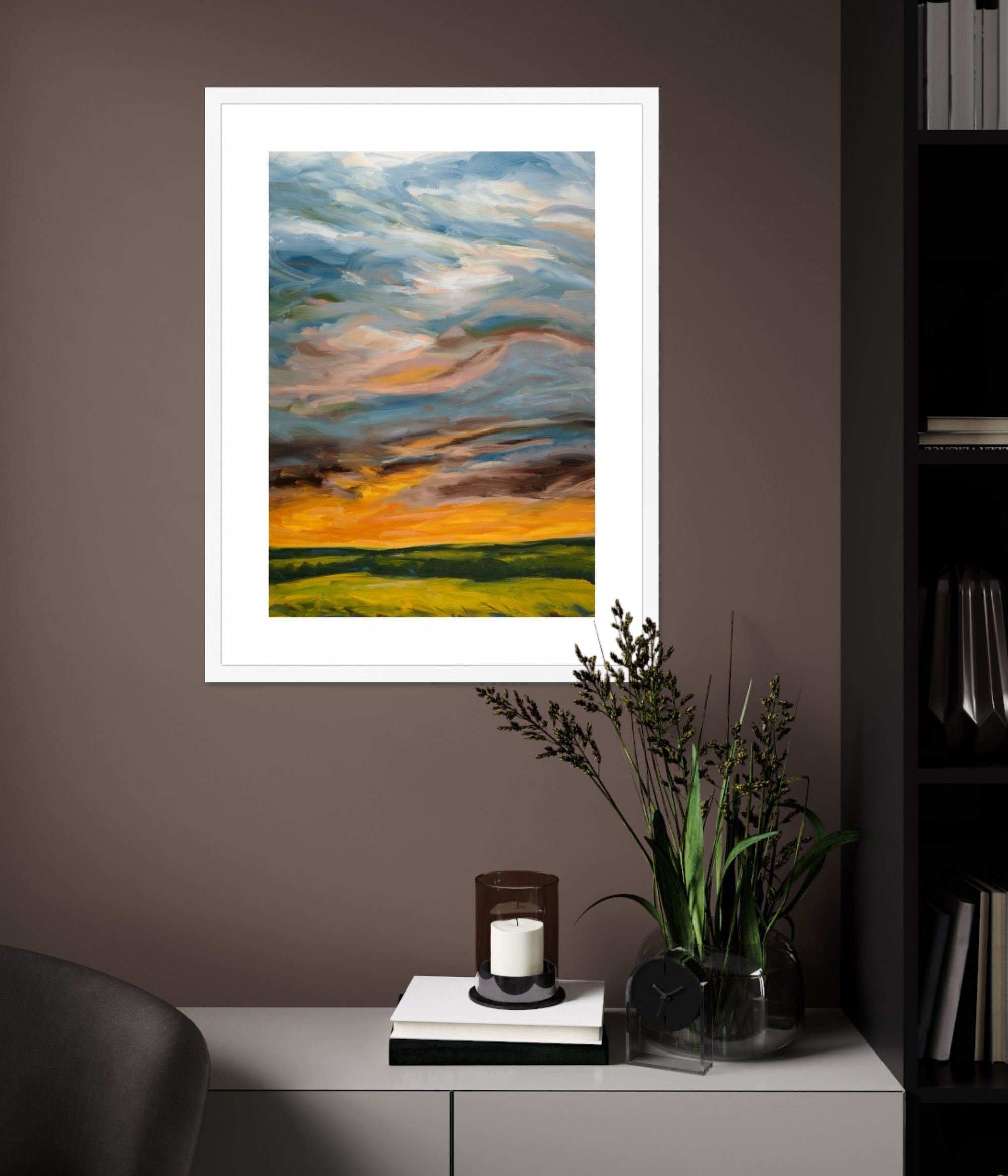 Framed abstract landscape painting on a wall with a candle and plant on a table below.