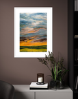Framed abstract landscape painting on a wall with a candle and plant on a table below.