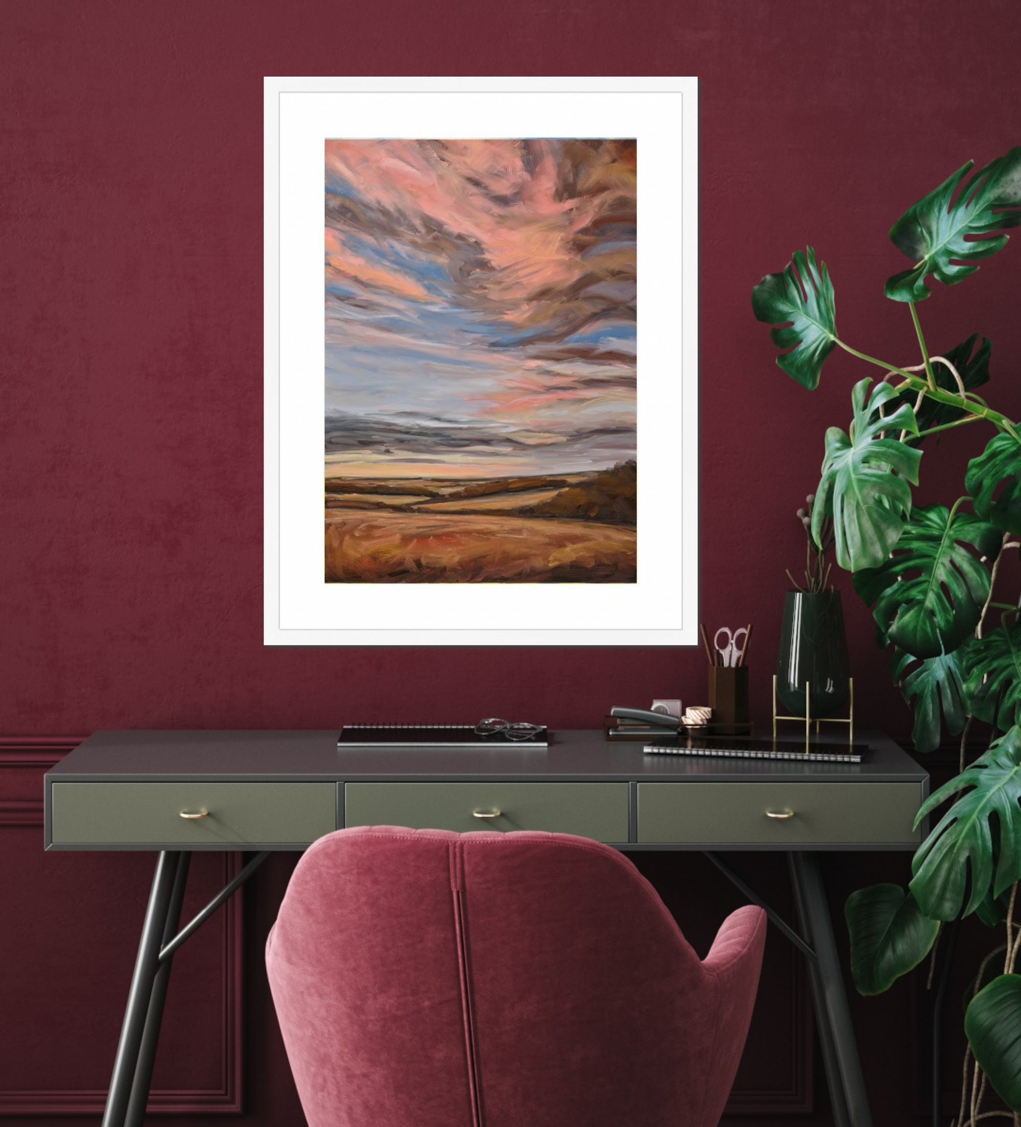 Artistic landscape print on a wall above a desk with a pink chair and plant.