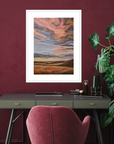Artistic landscape print on a wall above a desk with a pink chair and plant.