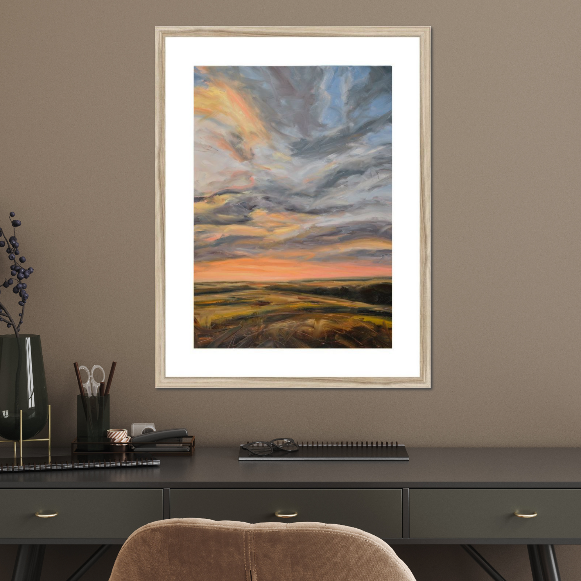 Framed artwork of a sunset over a field on a wall above a desk.