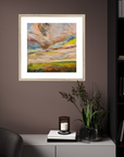 Framed abstract painting on a wall with a candle and plant on a table below.