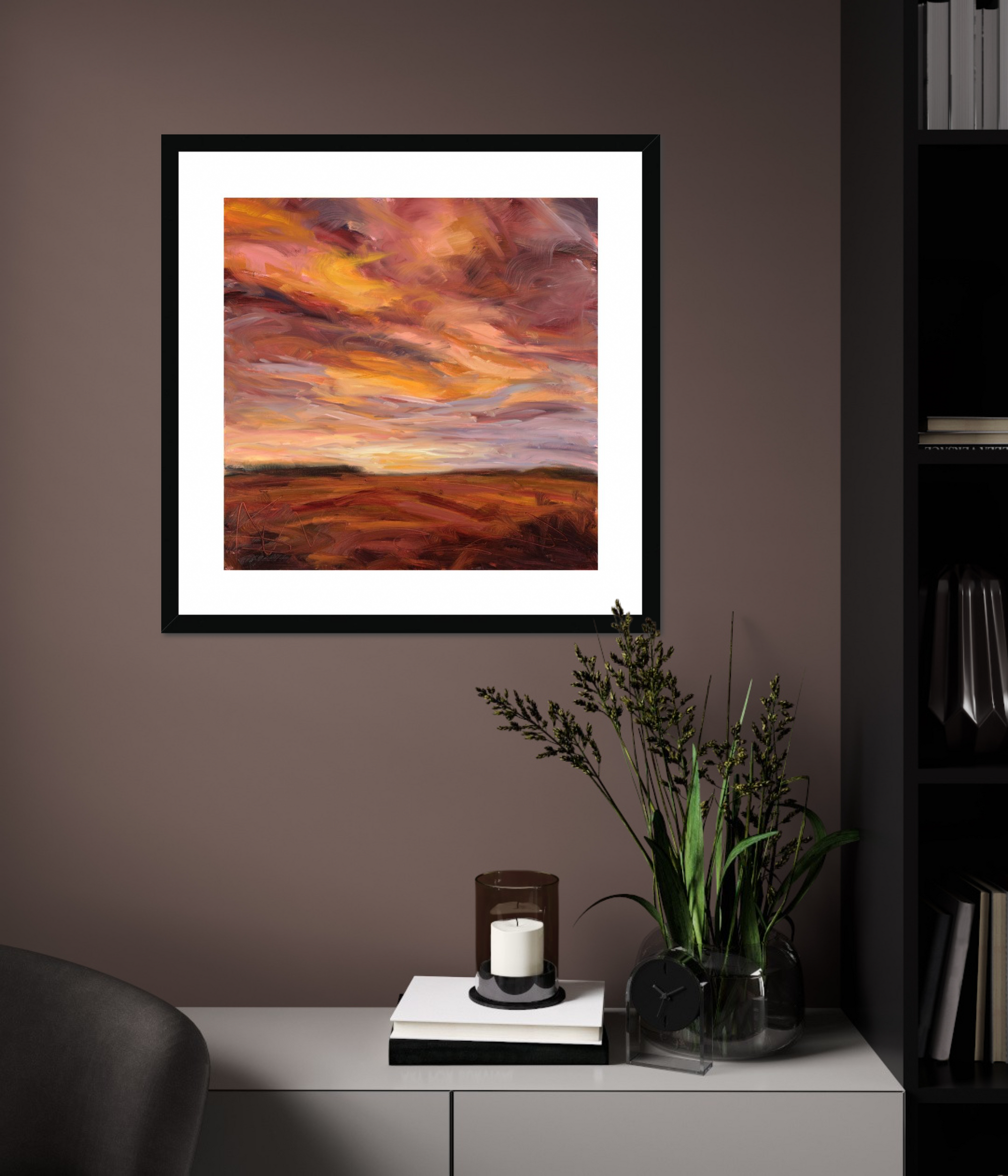 Framed artwork of a sunset over a landscape on a wall in a room with a cabinet and plant.