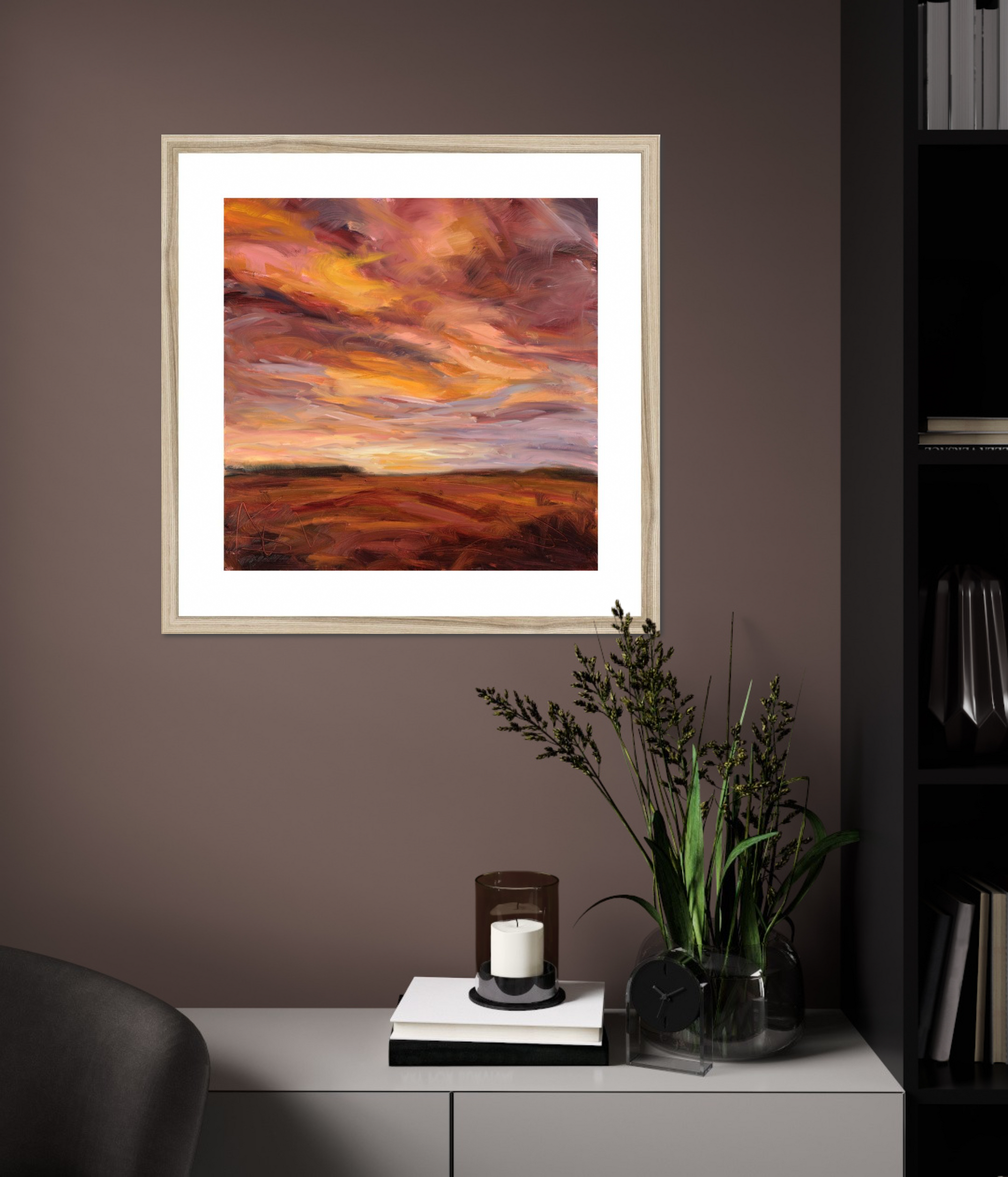 Framed artwork of a sunset over a landscape on a wall with decorative elements below.