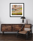 Wooden sideboard with a chair, lamp, and books against a white wall with a framed abstract painting.