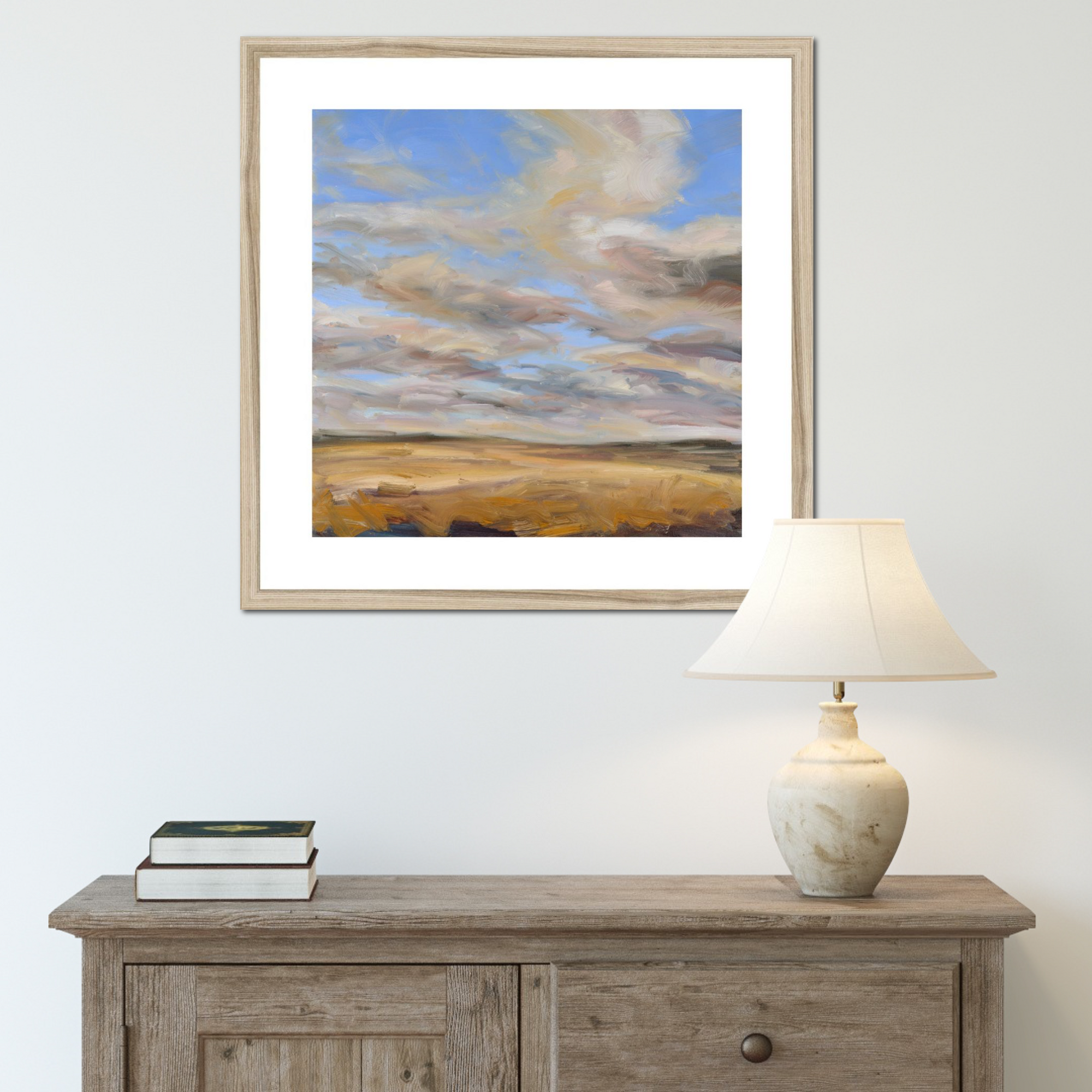 Framed landscape painting above a wooden console table with a lamp and books.