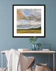 Framed landscape painting on a blue wall above a desk with decorative items.