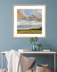 Framed landscape painting on a blue wall above a desk with decor items.