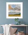 Framed landscape painting on a blue wall above a desk with decorative items.