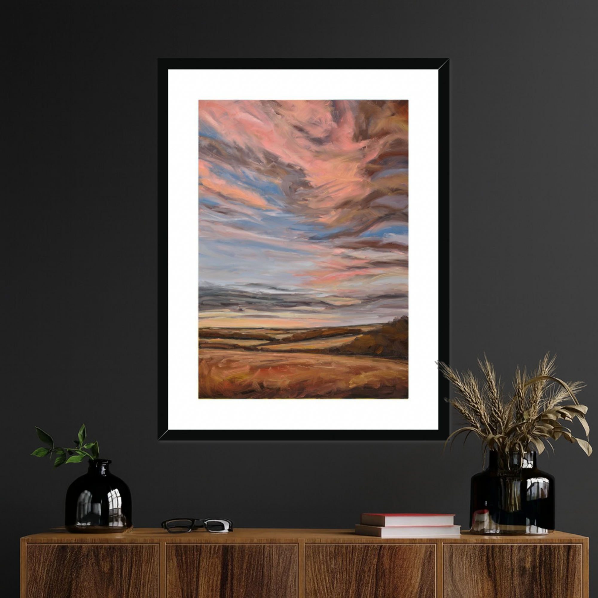 Framed artwork of a sunset over a field on a dark wall above a wooden console table.