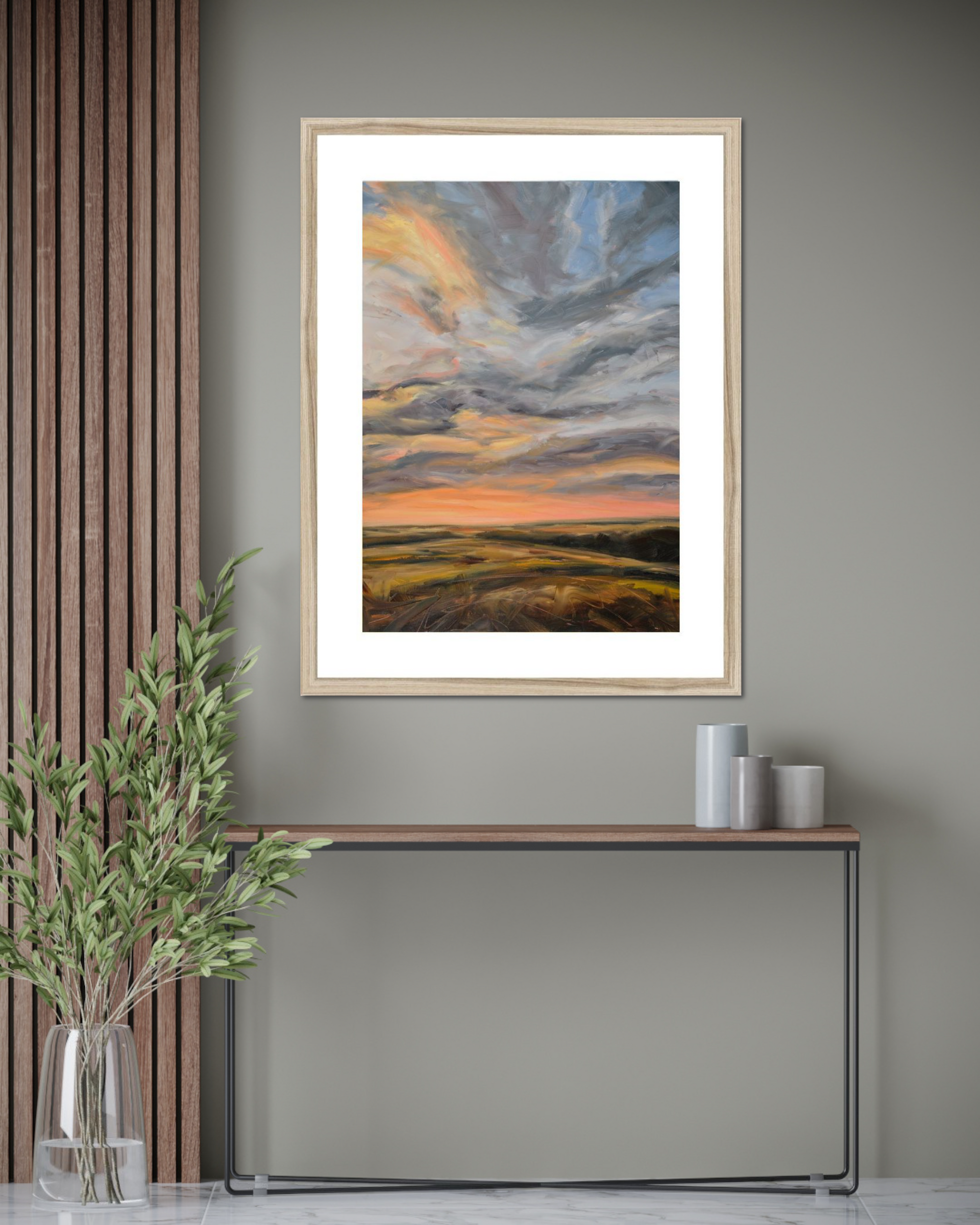 Framed artwork of a sunset over a field on a gray wall with decorative elements.