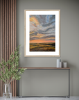 Framed artwork of a sunset over a field on a gray wall with decorative elements.