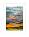 Framed abstract painting of a colorful sky with green fields below on a white background