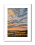 Framed artwork of a sunset with swirling clouds in a white frame.