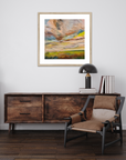 Wooden sideboard with a chair, books, and a lamp in a room with a framed abstract painting on the wall.