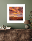 Framed abstract artwork on a wall above a wooden cabinet with books and a lamp.